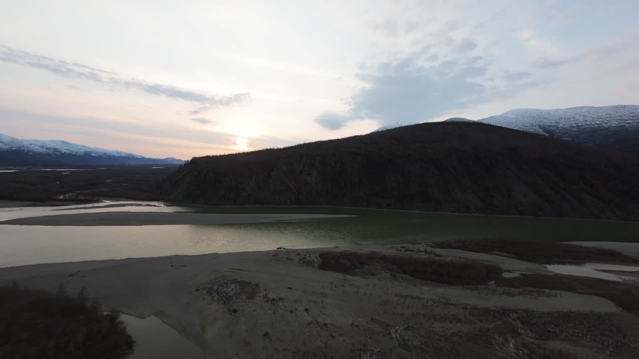 A breathtaking view unfolds as the golden sun dips below majestic mountains, illuminating serene rivers and lush landscapes in a symphony of color and nature's beauty.