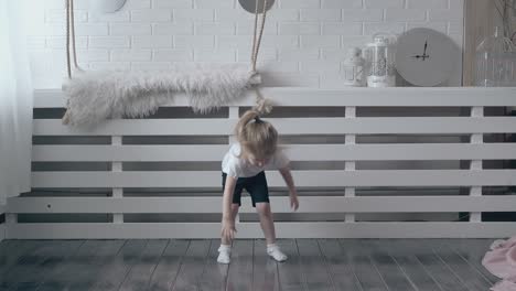 little-blond-girl-leans-forward-and-touches-wooden-floor