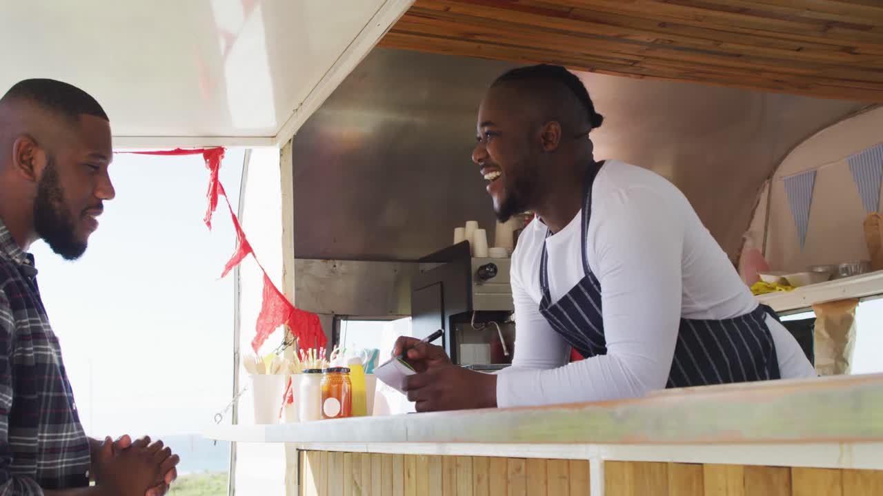hombre afroamericano con delantal ordenando comida en el camión de comida
