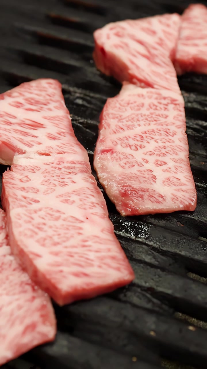 Primo piano di striscioline di manzo marmorizzato pregiato che sfrigolano su una griglia per barbecue in metallo nero.
