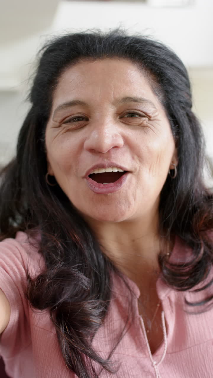 Happy biracial senior woman having video call and smiling in sunny room, slow motion