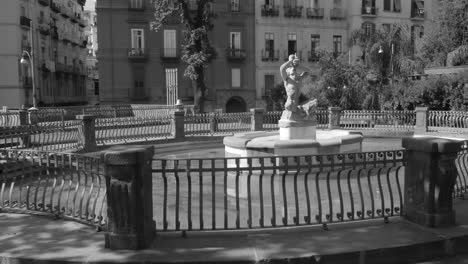 Fotografía-En-Blanco-Y-Negro-De-Una-Fuente-En-La-Entrada-De-Un-Parque-Rodeado-De-Casas-Residenciales-En-La-Histórica-Ciudad-De-Nápoles,-Italia