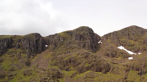 An-aerial-shot,-revealing-a-rocky-mountain-peak-with-patches-of-snow-|-The-Lost-Valley,-Glencoe,-Scotland-|-Shot-in-4k-at-30-fps