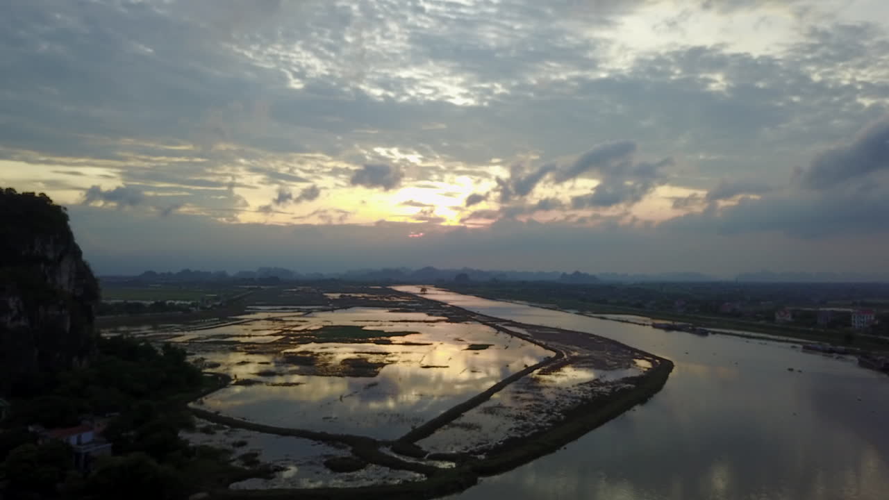 Experience a beautiful sunset over the flooded area of the Day River in Ninh Binh, Vietnam. The scene captures the serene reflections on the water and the tranquil landscape as day turns to dusk