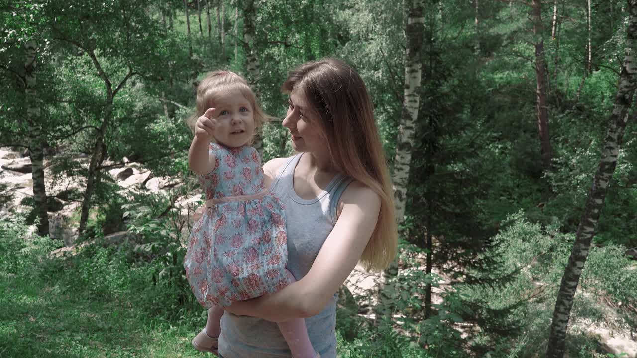 retrato de una hermosa madre joven con su hija en el bosque sobre un fondo de un río de montaña en primer plano