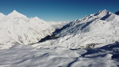 Un-Poco-De-Niebla-Viene-Del-Valle-A-Las-Montañas-Nevadas-En-Un-Clima-Soleado-En-Los-Alpes-Suizos,-Por-Drones