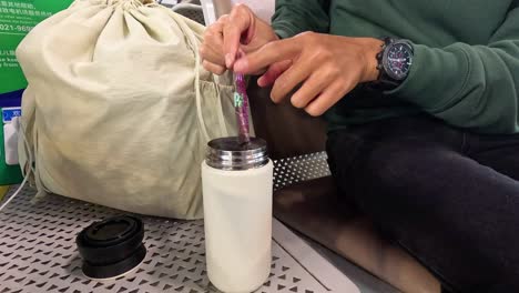 person mixes a beverage in a thermos while seated.