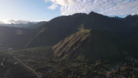 aerial of the town and mountains during sunrise with lens flare of urubamba, sacred valley, cusco, peru. drone pan crane up