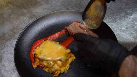 poniendo una rebanada de carne en un plato negro con macarrones y queso