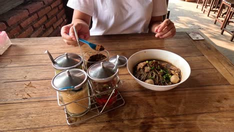 person seasoning noodle dish with condiments