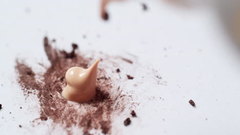 a close-up shot of a tube of liquid foundation concealer squeezed on a clean palette board to be mixed with some brown make-up tint