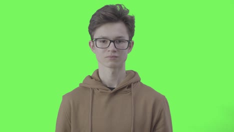 serious boy in eyeglasses making no gesture at green background. portrait of confident caucasian teenager disagree with something. objection, protest, disapproval. chromakey.