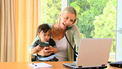 Mujer-Cargando-A-Un-Bebé-Y-Trabajando-En-Una-Computadora-Portátil.-