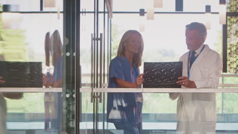médicos masculinos y femeninos con abrigos blancos y trajes de extirpación discutiendo la exploración del paciente en el edificio del hospital