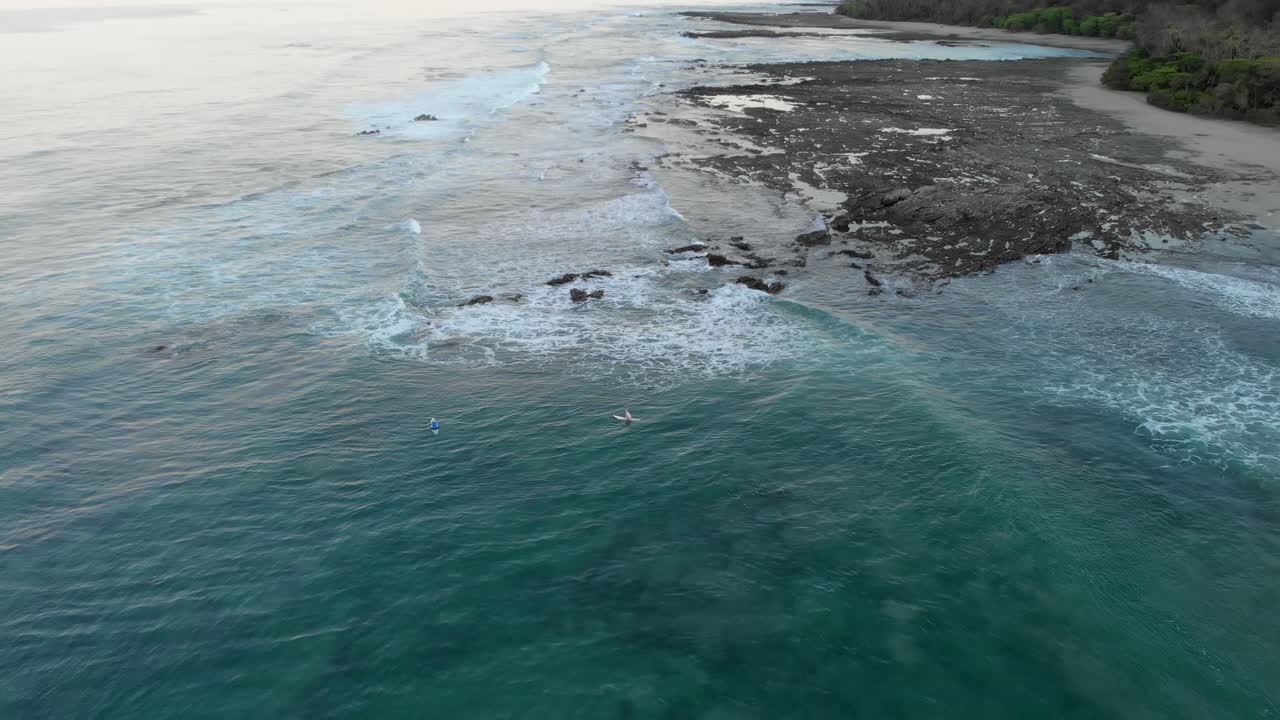 Orang-orang Menikmati di Papan Selancar Mengambang di Atas Samudra Biru Tenang dengan Terumbu Karang Bawah Air di Sebuah Pulau di Kosta Rika - Rekaman Udara