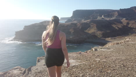 young woman walks to the end of the cliff and looks at the beach and the views