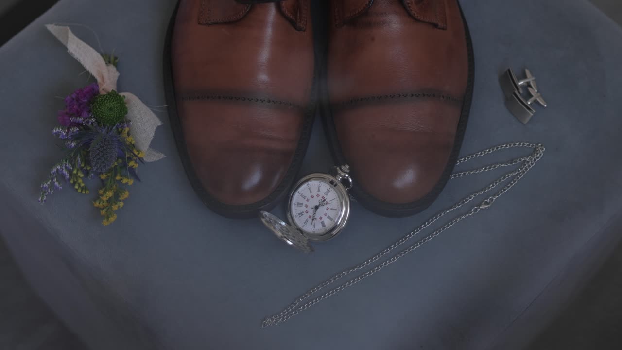 brown leather shoes pocket watch boutonniere and cufflinks arranged neatly on soft fabric