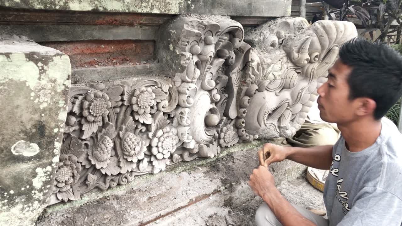 Asian man sculpting detailed patterns of a Hindu temple in the busy streets of Ubud, Bali