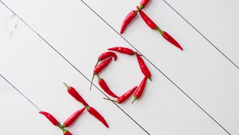 a word hot formed with small red chilli peppers  placed on white wooden table