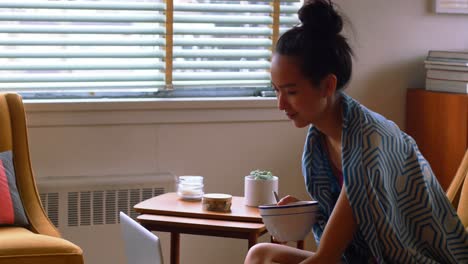 beautiful woman having cereal while using laptop