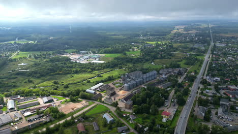Drone shot of industrial area of a city with highway on the side on a cloudy day, with nature and trees surrounding it