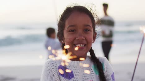 Porträt-Eines-Glücklichen-Hispanischen-Mädchens,-Das-Bei-Sonnenuntergang-Am-Strand-Mit-Wunderkerzen-Spielt