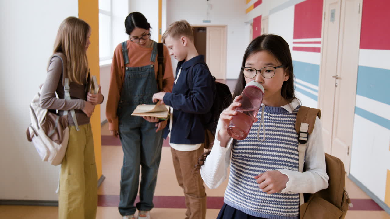 Students in a school hallway with one girl drinking water
