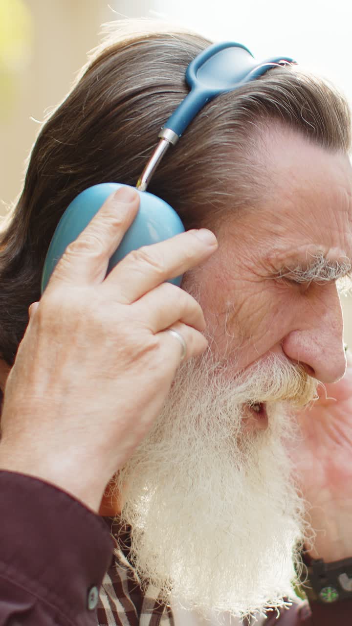 Vecchio anziano felice con le cuffie wireless che sceglie di ascoltare musica ballando all'aperto per la strada della città