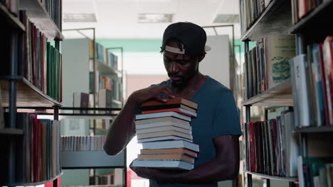 Un hombre negro sostiene libros apilados en el pasillo de una biblioteca, mirando pensativo hacia la estantería, decidiendo cuál será su próxima elección, con gorra informal y camiseta, ambiente de estudio, enfoque académico, búsqueda de conocimiento
