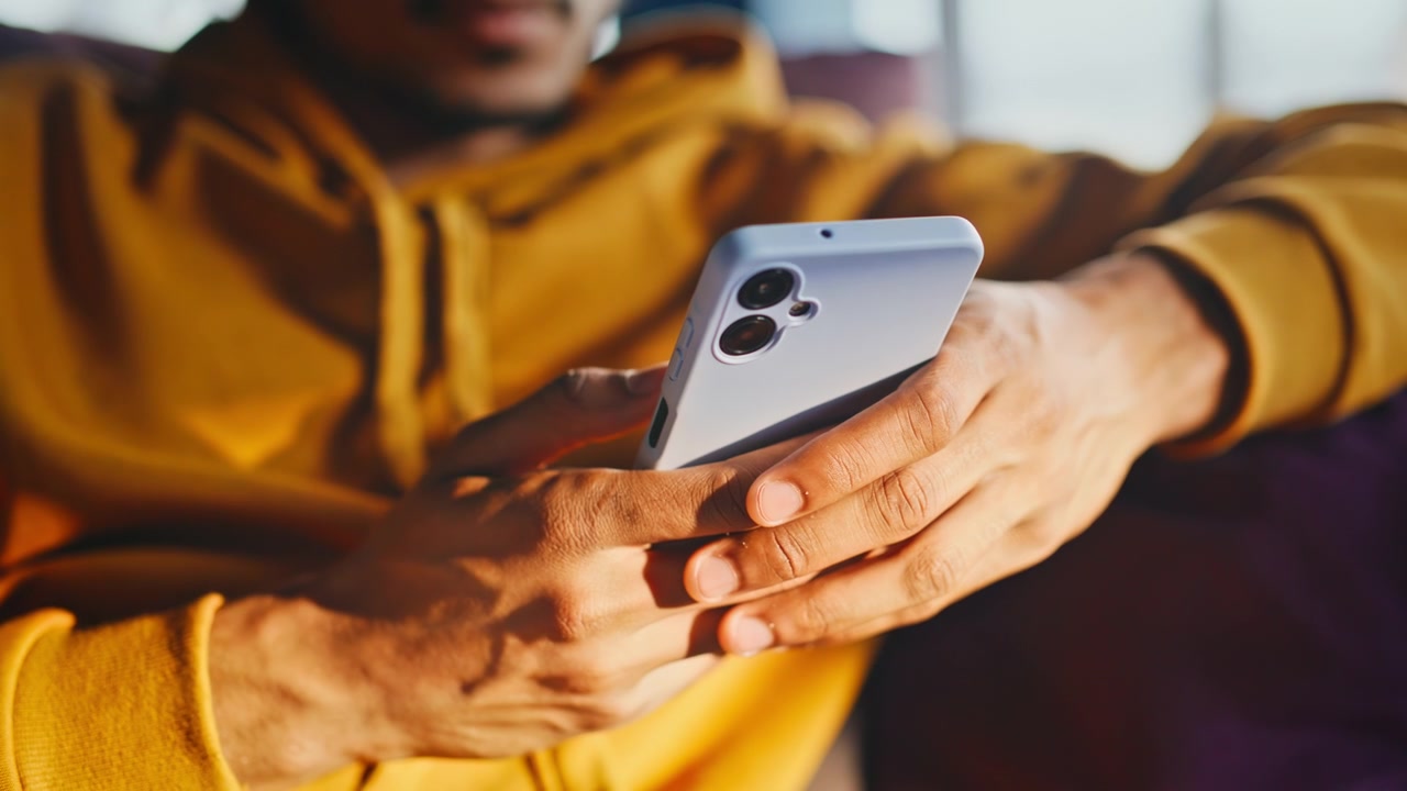 Primo piano di mani che tengono uno smartphone. Uomo afroamericano che scorre sul divano di casa