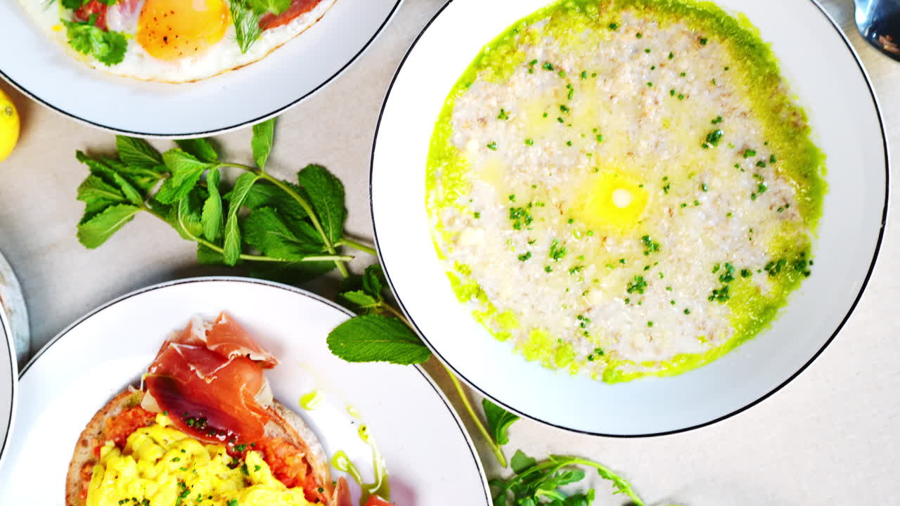 Multiple plates of various Eastern European breakfast foods, including porridge, eggs, pancakes, and crepes, are arranged on a table, creating a visually appealing spread
