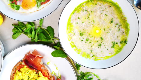 multiple plates of various eastern european breakfast foods, including porridge, eggs, pancakes, and crepes, are arranged on a table, creating a visually appealing spread