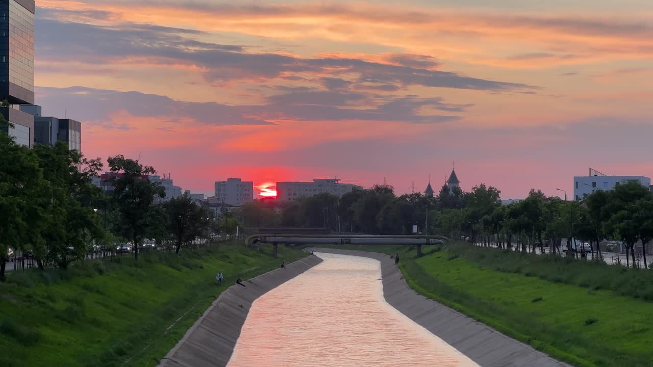 Video of sunset over the Bahlui River in Iași, featuring orange skies, a church spire, and riverbanks