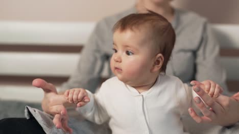 little beautiful baby girl holding her mother's fingers trying to sit down