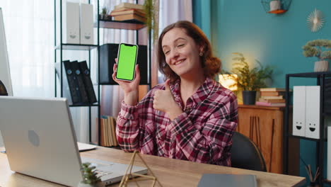 woman freelancer looking at camera and showing smartphone with green screen for new application