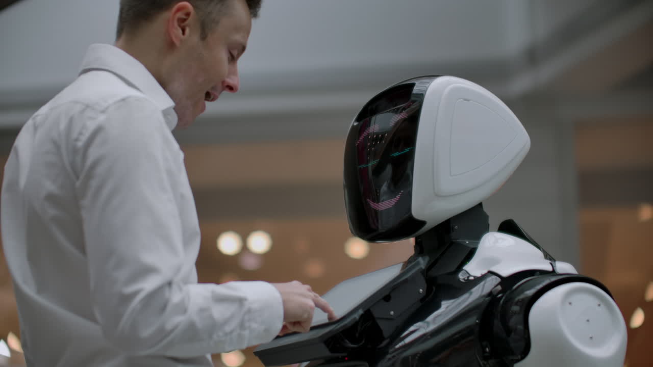 un hombre se para con un robot bot y le hace preguntas y pide ayuda haciendo clic en la pantalla en el cuerpo del robot. la interacción humano-robot en el mundo moderno