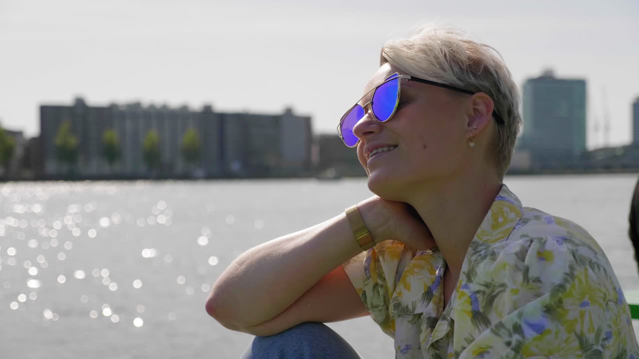 Confident young woman soaks in the summer sun, bay and city in the background.