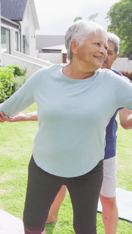 vertical video of happy senior biracial couple practicing yoga in garden