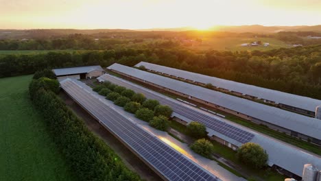 long barn buildings in american countryside at sunset. aerial backwards shot. modern solar panels covering roofs. green energy theme in rural area of usa.