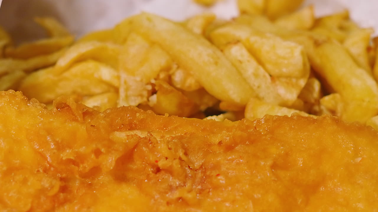 Slow Moving Camera View Over Traditional British Fish and Chips Meal in Takeaway White Paper. Deep Fried Fresh Cod Seafood Served in Britain