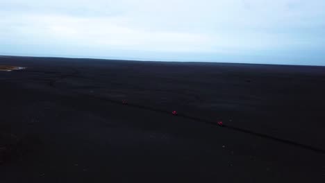 aerial view of red quad bikes speeding off road through iceland black sand beach