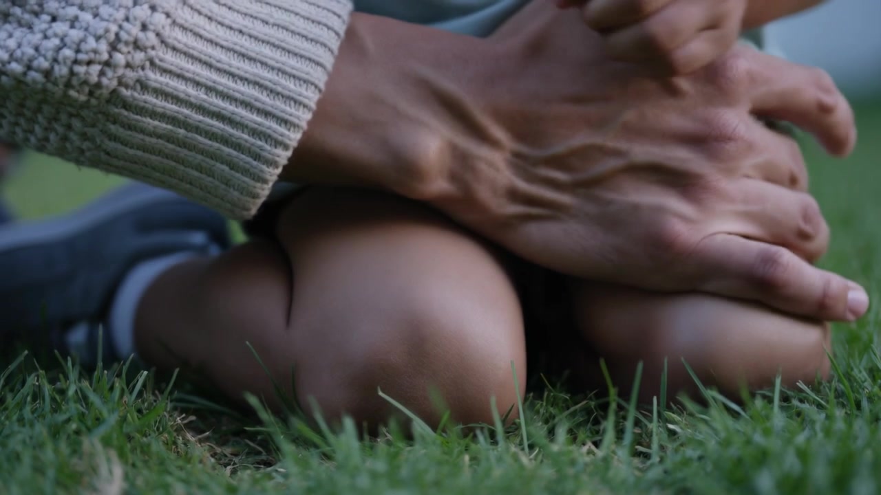 Bambino inginocchiato in giardino che nota una cavalletta e si protende all'altezza del ginocchio, mentre un adulto lo copre per proteggerlo.