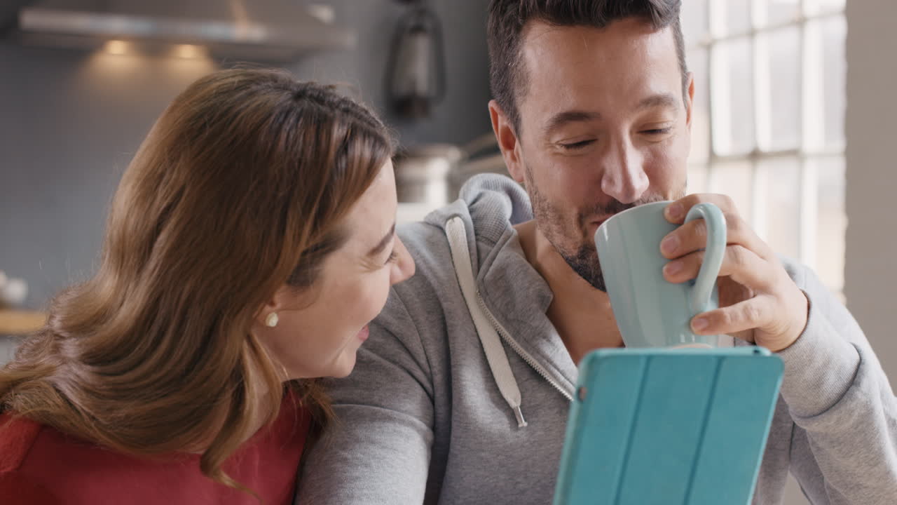 집에서 디지털 태블릿을 사용하는 커플이 즐겁게 커피를 마시고 있습니다.