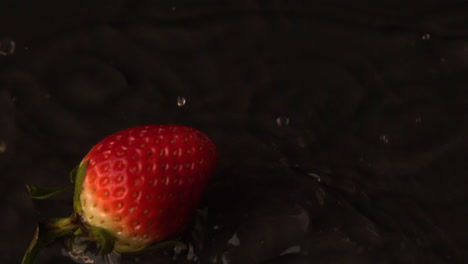 strawberry falling on wet black surface