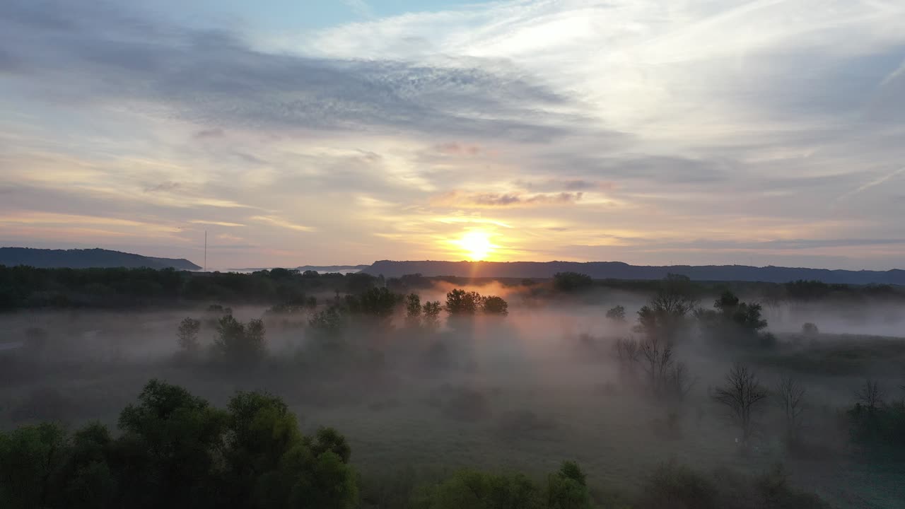 Ilmakuva sumuisesta laaksosta auringonnousun aikaan, lentävine lintuineen