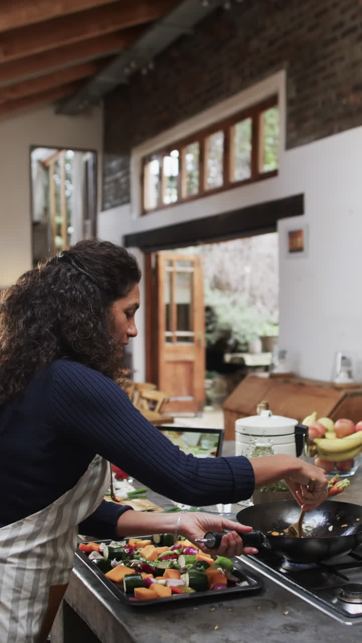 Vertical video of biracial woman in apron preparing meal in kitchen, slow motion