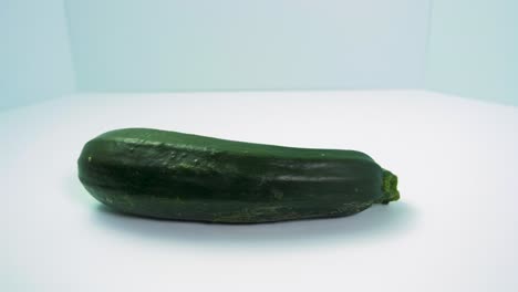 green fresh zucchini squash rotates on a light blue background, healthy food, concept, medium close up shot camera rotate right