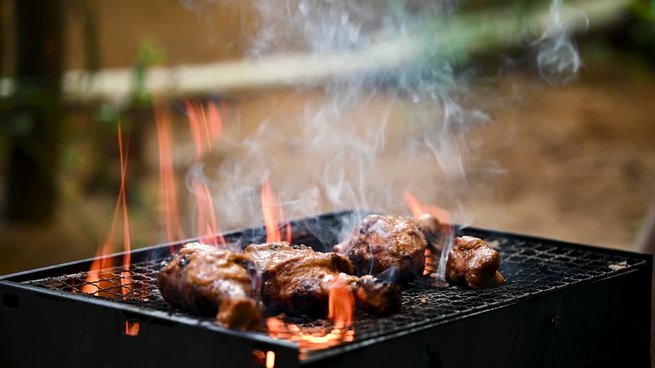 Slow-motion wide shot of marinated chicken drumsticks sizzling over high flames on a backyard BBQ grill. Juicy chicken and dramatic fire create appetizing outdoor cooking scene for food and health