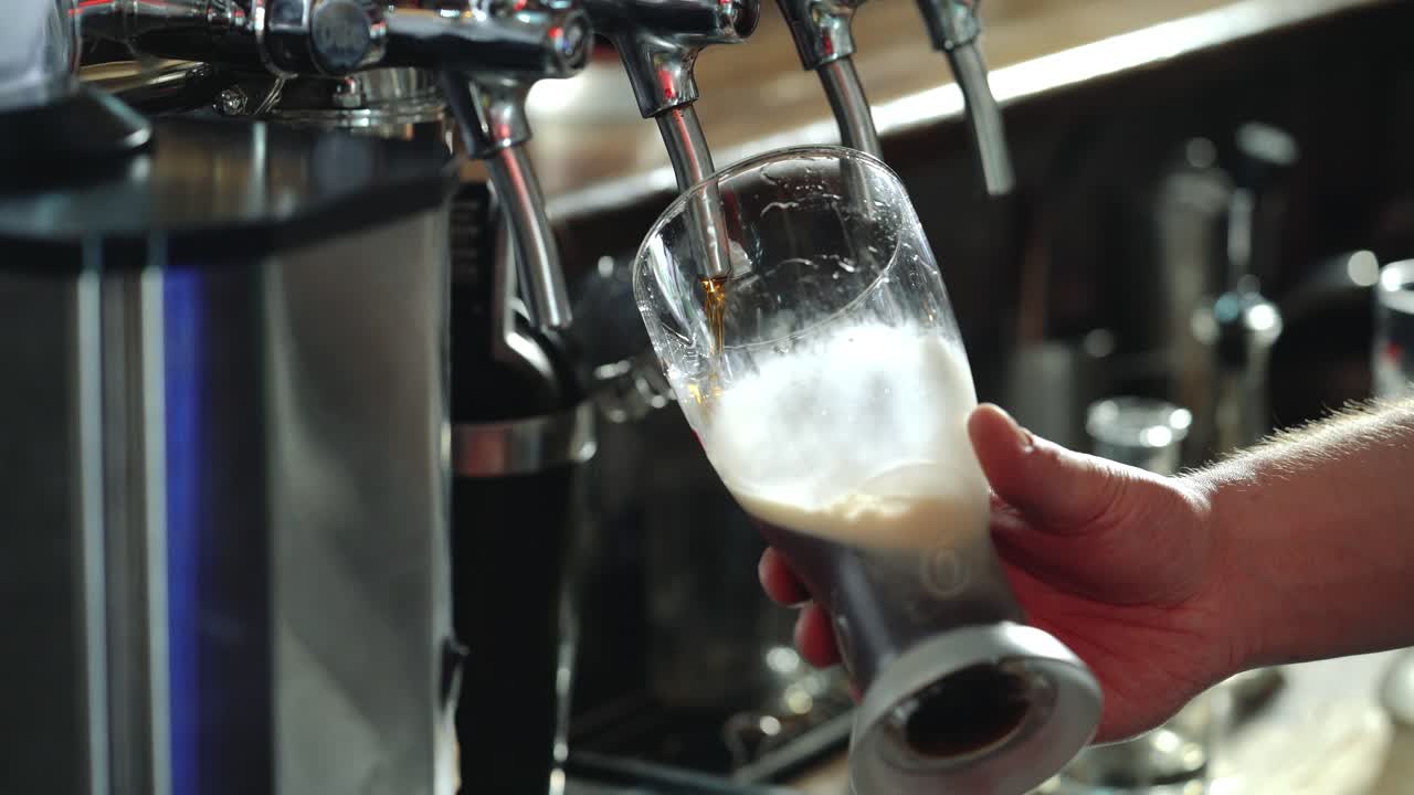 Bartender pours a dark beer in glass. Close-up.