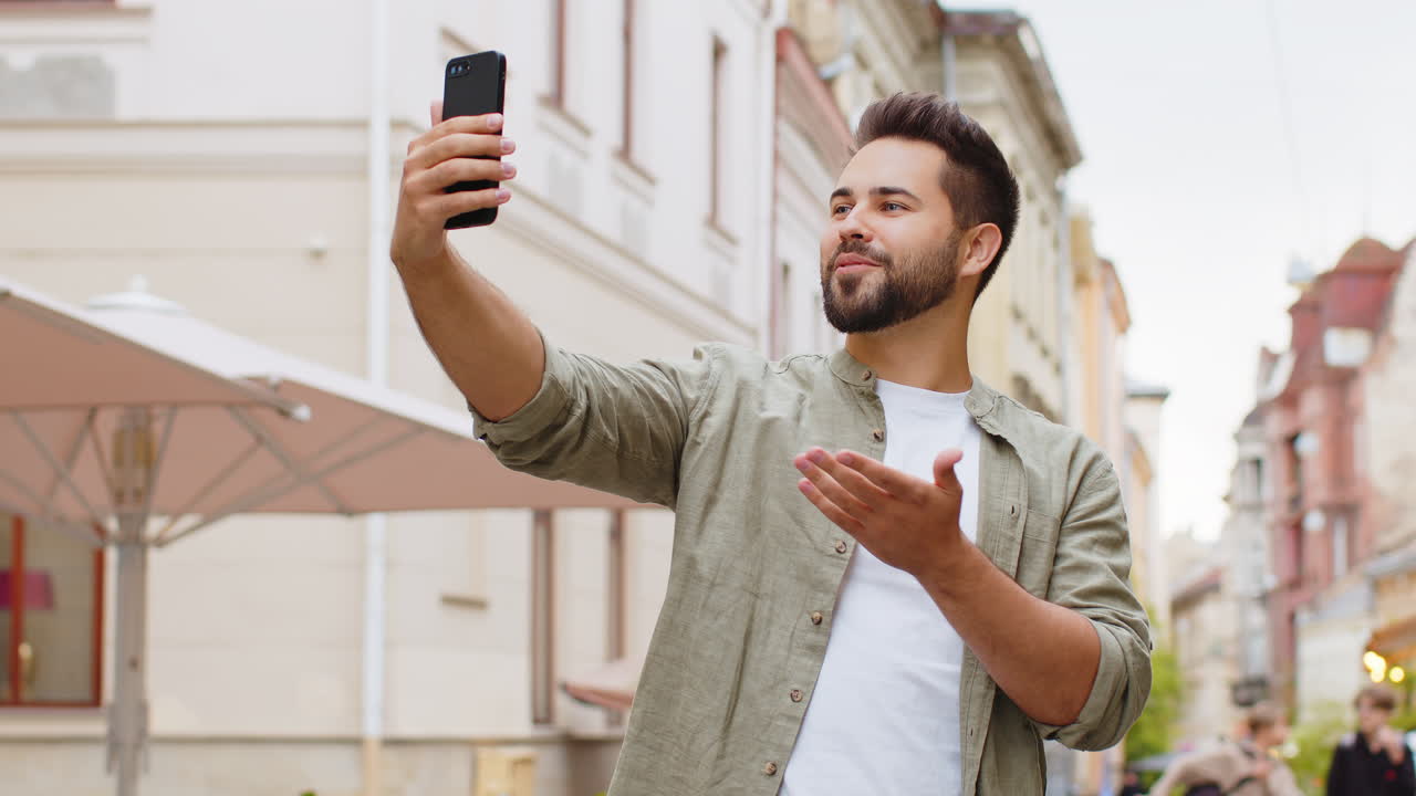 Young man blogger taking selfie on smartphone video call online with subscribers in city street